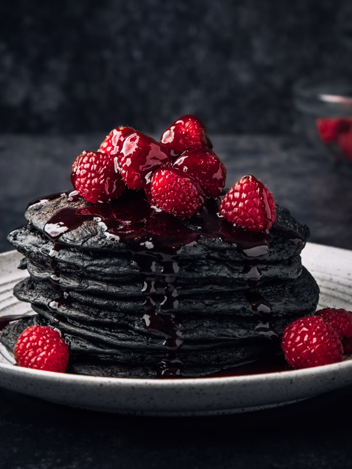 These charcoal pancakes are served with a bright raspberry sauce, creating a striking red-and-black contrast that makes them perfect for dramatic brunch presentations.